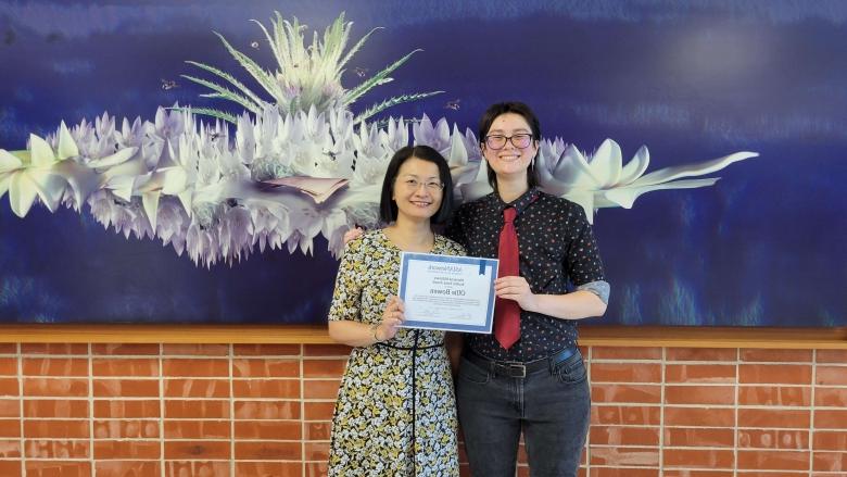 A student 和 a faculty member pose for a photo with an award.